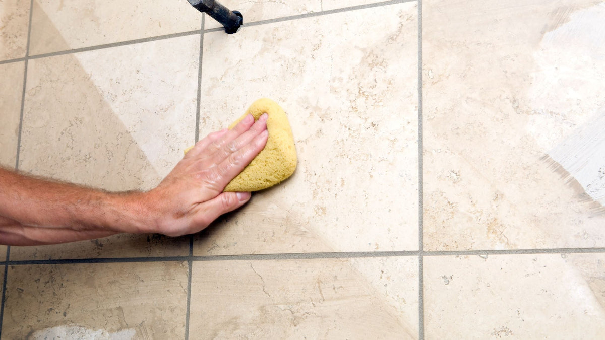 Hand wiping grout on bathroom wall